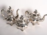 three silver teapots on a white table with a white background