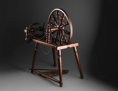un vieux rouet posé sur un support en bois, sur fond noir