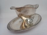 a silver sauce boat on a silver plate on a white table
