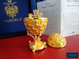 un calice en or et un œuf en or posés sur une table rouge