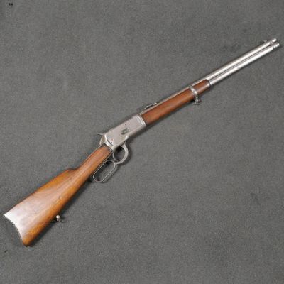 un fusil avec une crosse en bois posé sur une surface grise