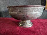an antique silver bowl on a red table cloth with a picture in the background