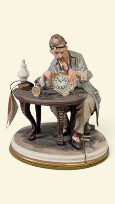 une figurine représentant un homme assis à une table avec une horloge