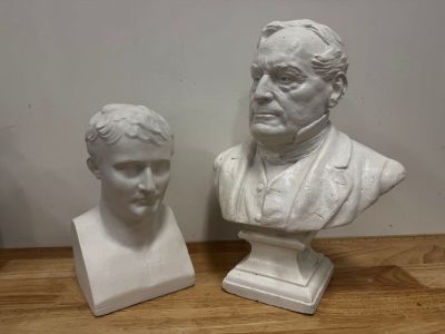 two white busts of men sitting next to each other on a wooden table