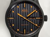 un gros plan d'une montre noire avec des aiguilles orange sur un fond blanc