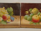 two paintings of fruit are displayed on a wooden surface