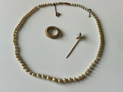 un collier de perles, accompagné d'une bague et d'une broche, posé sur un fond blanc