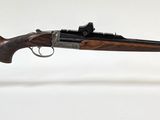 Le fusil est exposé sur un socle en acrylique transparent.