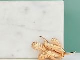 broche en feuille d'or posée sur un bloc de marbre blanc