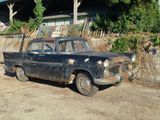 une vieille voiture rouillée garée devant un immeuble entouré d'une clôture en bois