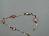 un gros plan sur un bracelet à chaîne en or orné de perles roses et blanches