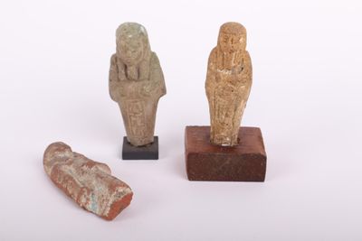 trois figurines de l'Égypte antique posées sur des socles en bois, sur une surface blanche