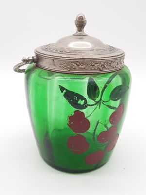 un bocal en verre vert muni d'un couvercle argenté orné de cerises