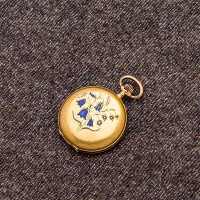 une petite montre de poche en or ornée d'une fleur bleue