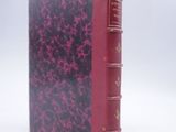 an old book with a red cover sitting on top of a white surface