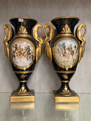 une paire de vases noirs et dorés ornés de peintures, posés sur une table en verre