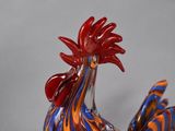 a glass rooster figurine with a red and blue tail