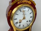 a red and gold clock with roman numerals on it