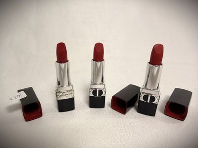 three red lipsticks are lined up on a white surface