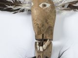 a wooden mask with feathers on it on a white surface