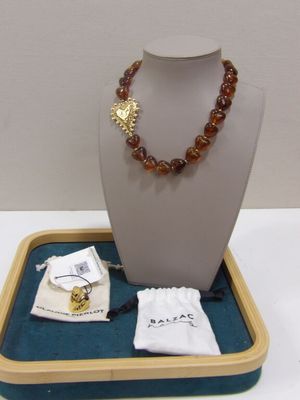 un collier présenté sur un présentoir, à côté d'un sac contenant des bijoux