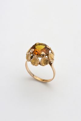 une image représentant une bague en or sertie d'une citrine facettée entourée de feuilles