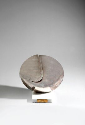 sculpture en argent représentant un objet circulaire posé sur une surface blanche