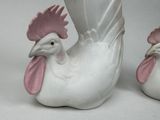 pair of white ceramic roosters with pink beaks on a white background