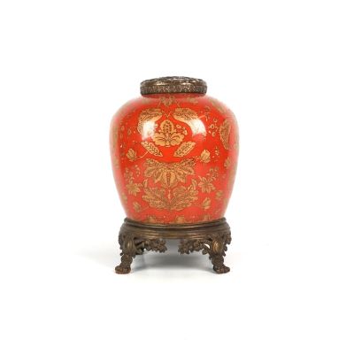 un vase rouge orné de motifs dorés, posé sur un socle