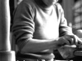 une photo en noir et blanc d'une femme assise à une table, en train de travailler sur un morceau de bois