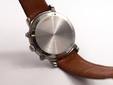 the watch is sitting on a white surface with a brown strap