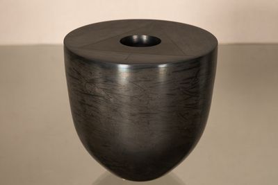 un vase noir posé sur une table, avec un mur blanc en arrière-plan