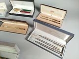 many different pens and pencils in boxes on a table