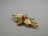 a close up of a gold bee brooch with a red stone
