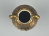 a gold vase with a black center sitting on a white surface