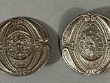 deux boutons en argent ornés de motifs, posés sur une table