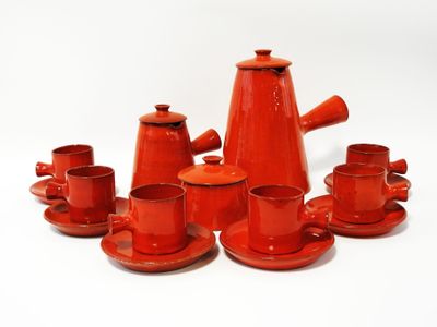 un service à thé rouge avec des tasses et des soucoupes posées sur une surface blanche