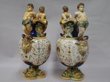 two vases with figurines sitting on top of them on a white surface