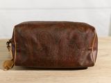 the brown leather toilet bag is sitting on a wooden table