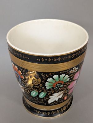 un gros plan d'une tasse noire et dorée ornée de fleurs