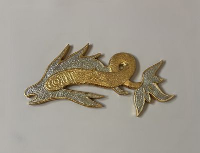 a gold and silver fish brooch on a white surface