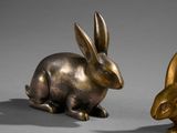 pair of bronze rabbits sitting next to each other on a gray surface