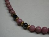 Collier de perles roses et noires rehaussé de touches dorées sur un fond blanc