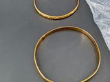 two gold bracelets on a table with a plastic bag in the background