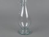 a clear glass vase with a handle on a gray surface