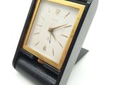 une petite horloge noire avec un cadran doré sur un fond blanc