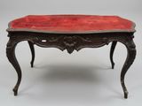 an old table with a red velvet top and ornate legs