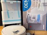 une image représentant un robot blanc et bleu posé sur une table en bois, à côté d'une boîte