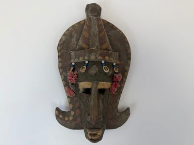 un vieux masque en bois accroché à un mur sur fond blanc