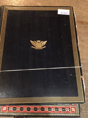 an old black book with a gold emblem on it sitting on a wooden table